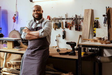 Portrait of smiling african american carpenter preparing to start production in messy furniture...