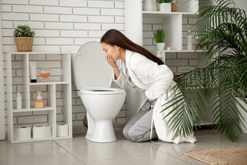 Sick young Asian woman near toilet bowl in restroom