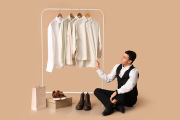 Handsome young happy man and rack with clean shirts on brown background