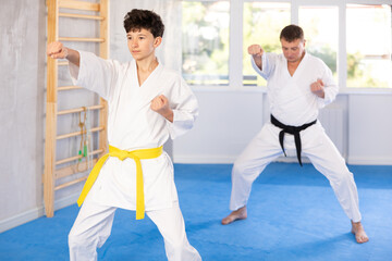 Adult man and boy teenager in kimono practice karate technique in gym