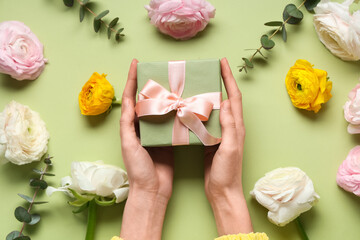 Female hands with gift box, beautiful ranunculus flowers and eucalyptus on green background
