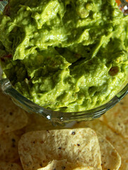 A bowl of green guacamole sits next to a plate of tortilla chips. The bowl is filled with a thick, creamy green dip that looks delicious and inviting