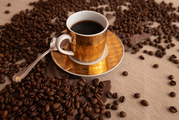 A cup of coffee is sitting on a saucer with a pile of coffee beans around it. Concept of relaxation and comfort, as the coffee is a common beverage associated with winding down