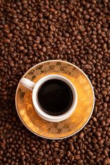 A cup of coffee sits on a saucer on a table covered in coffee beans. Concept of warmth and comfort,...