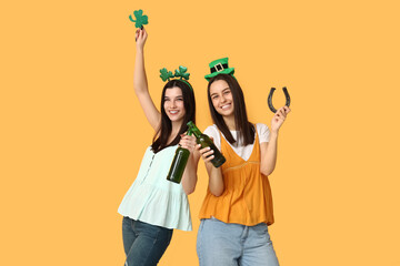 Beautiful young women with bottles of beer, clover and horseshoe on yellow background. St....