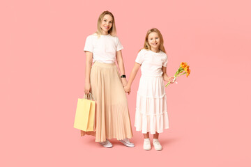 Cute little girl and her mom with shopping bags and bouquet for Mother's Day holding hands on pink background