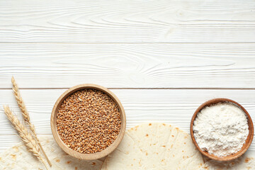 Composition with thin lavash, flour and bowl of wheat grains on light wooden background