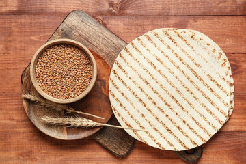 Composition with thin lavash and wheat grains on wooden background