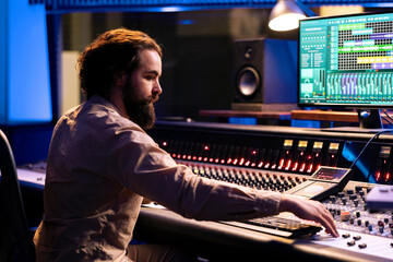Portrait of music producer working in control room with sliders and switchers, adjusting volume...