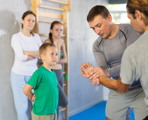 Obraz premium In gym at self-defense training, trainer on man explains technique of palm grip, boy, girl and woman are trained