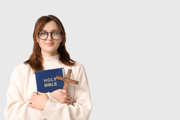 Religious young woman with Holy Bible and cross on white background