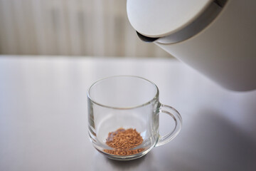 Woman stirs instant coffee in glass mug with boiled water on grey stone table