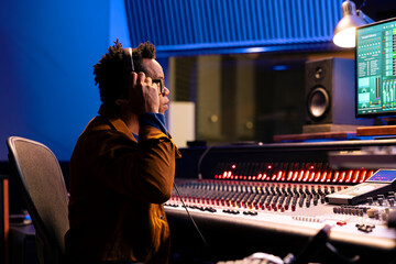 African american tracking engineer processing and editing music in studio control room, operating...