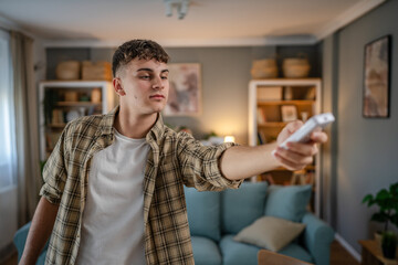 Young caucasian teenage man use remote control for TV or air-condition