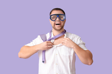 Happy office worker in diving mask takes off his shirt on lilac background