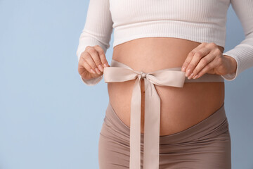 Young pregnant woman with bow on her belly against blue background, closeup