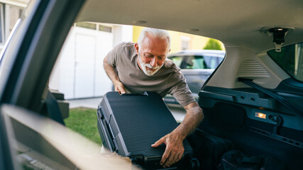 One senior man travel concept male put suitcase in trunk of the car