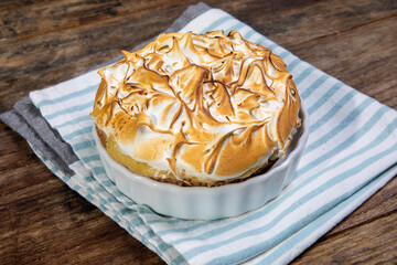 A Coconut cream pie or tart with flamed caramelized meringue on a blue cloth on a wooden table