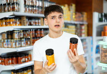 Young guy chooses of spices between two options while standing in supermarket