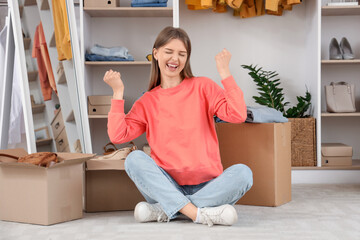 Beautiful young happy woman with wardrobe boxes and stylish clothes sitting in dressing room