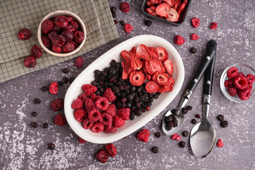 Bowls with different freeze-dried berries and spoons on grey background