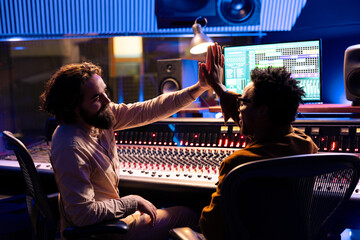 Pleased musician doing high five gesture with producer after finishing musical project, recording...