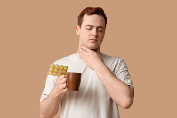 Young man with sore throat, hot tea and pills on beige background