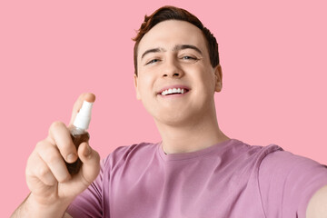 Young man with sanitizer taking selfie on pink background