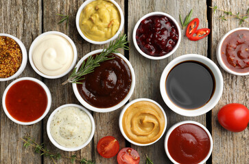 Different tasty sauces in bowls and ingredients on wooden table, flat lay