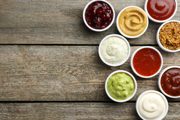 Different tasty sauces in bowls on wooden table, flat lay. Space for text
