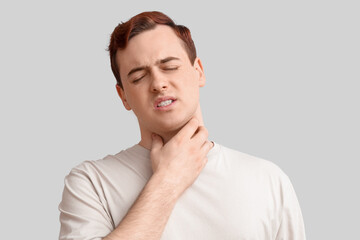 Young man with sore throat on light background