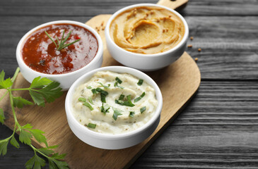 Different tasty sauces in bowls and parsley on black wooden table, closeup