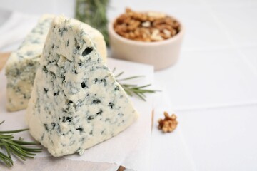 Tasty blue cheese with rosemary and walnuts on white tiled table, closeup. Space for text