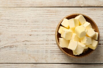 Tasty butter cubes in bowl on light wooden table, top view. Space for text