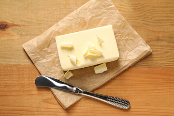 Tasty butter and knife on wooden table, top view