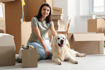 Fototapeta premium Young happy woman and cute Labrador dog with boxes on moving day sitting at home