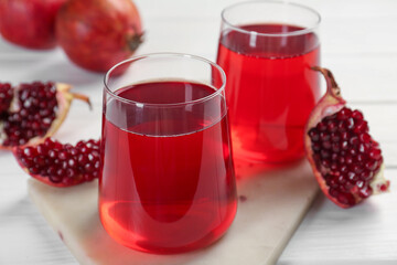 Tasty pomegranate juice in glasses and fresh fruits on white wooden table, closeup