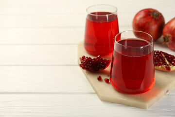 Tasty pomegranate juice in glasses and fresh fruits on white wooden table, closeup. Space for text