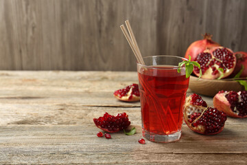 Tasty pomegranate juice in glass and fresh fruits on wooden table. Space for text