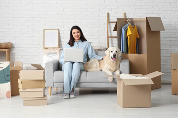 Young happy woman and cute Labrador dog with moving boxes sitting on sofa at home