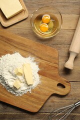Board with fresh butter and flour on wooden table, flat lay