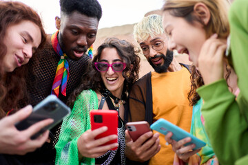 Surprised multiracial smiling group young generation z leaning brick wall using phones outdoors. Friends having fun together looking at social media. Concept of relationships and new technologies.