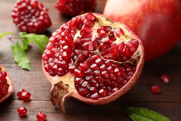 Cut fresh pomegranate and green leaves on wooden table, closeup
