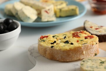 Tasty butter with olives, chili pepper and bread on white table, closeup