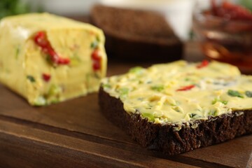 Tasty butter with green onion, chili pepper and rye bread on wooden board, closeup
