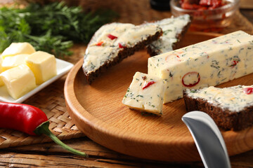 Tasty butter, dill, chili pepper and rye bread on wooden table, closeup