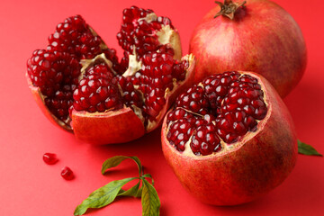 Fresh pomegranates and green leaves on red background