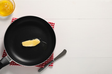 Melting butter in frying pan and knife on white wooden table, top view. Space for text