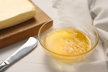 Melted butter in glass bowl and knife on white wooden table, closeup