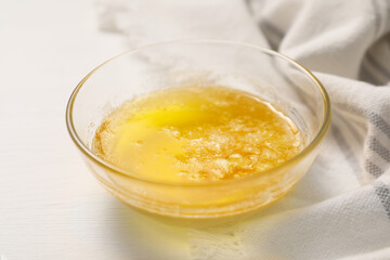 Melted butter in glass bowl on white wooden table, closeup